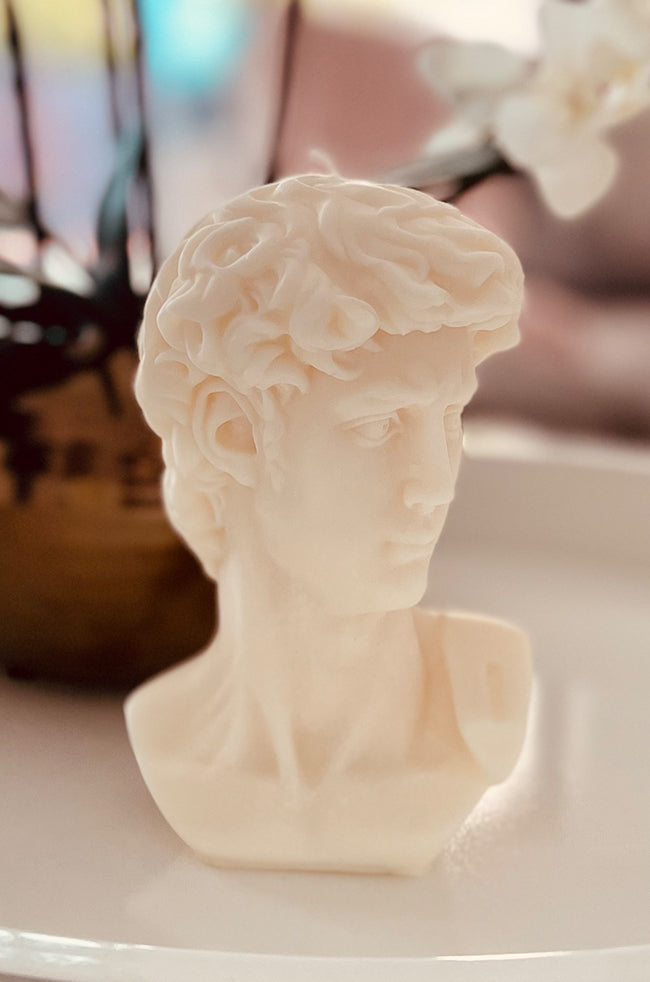 The Light of David Candle: Side view of The Light of David ivory bust candle displayed on a white surface with soft floral décor.