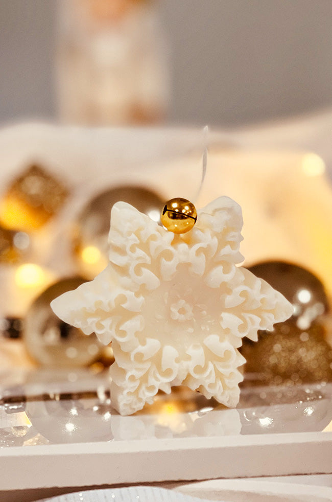 The Renaissance Snowflake Candle: Ivory Renaissance Snowflake sculptural Christmas candle with intricate floral details and a gold bell on top.