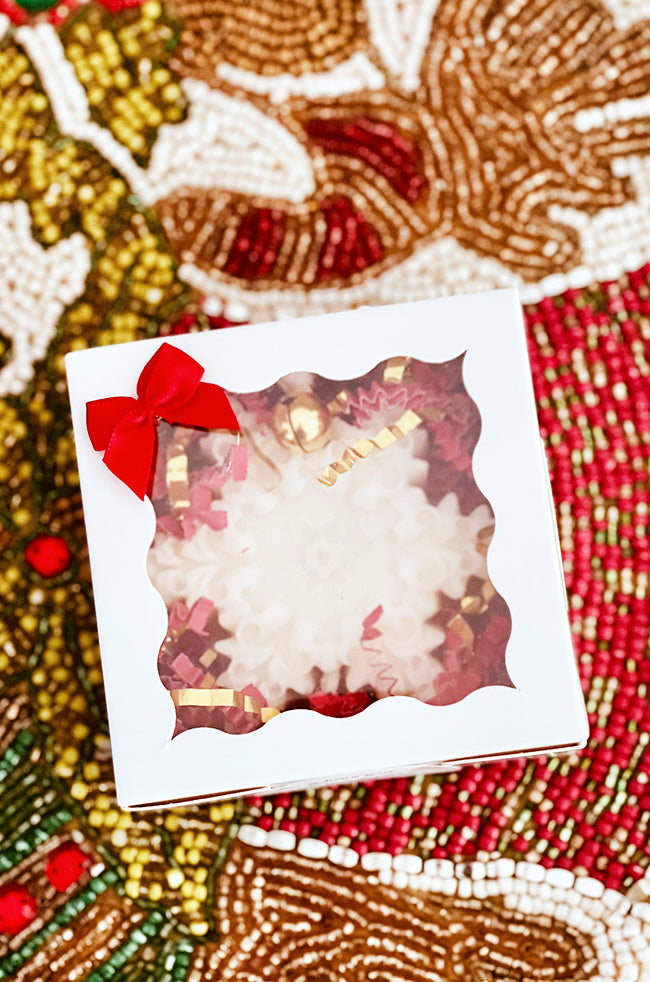 The Renaissance Snowflake Candle: Renaissance Snowflake candle packaged in a white gift box with clear window, red bow, and festive holiday filler.