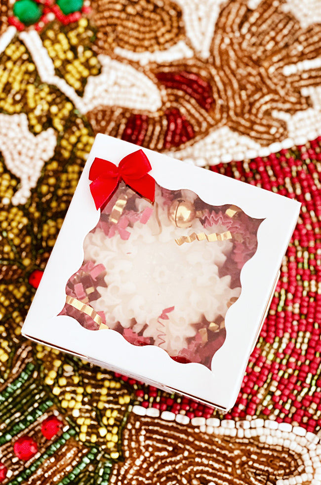 The Renaissance Snowflake Candle: Boxed Renaissance Snowflake Christmas candle with red bow and clear window, styled on a festive beaded holiday background.