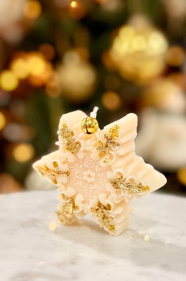 The Renaissance Snowflake Candle: Angled view of the Renaissance Snowflake sculptural candle decorated with gold flakes and topped with a gold bell.